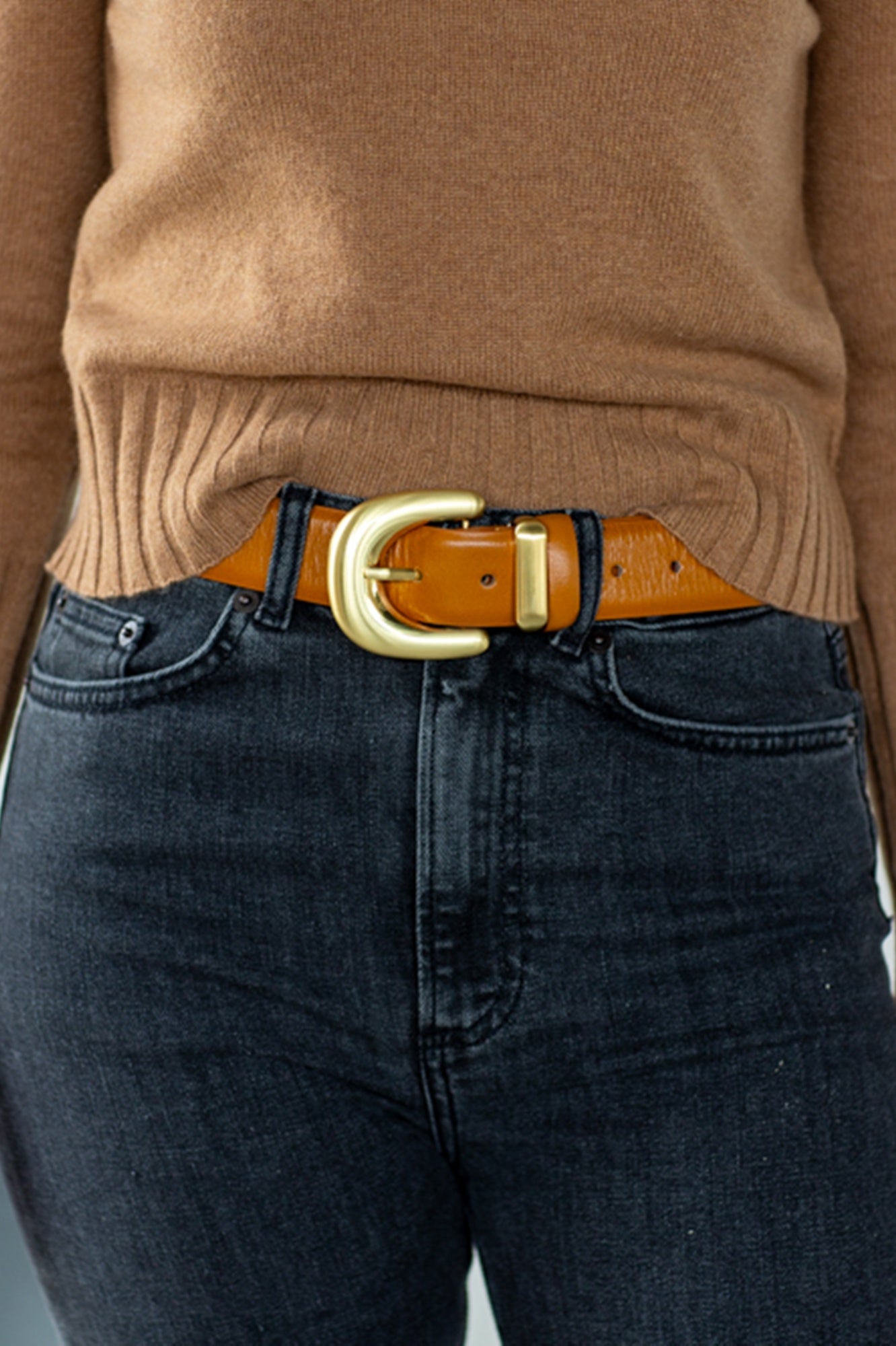 Person wearing a brown sweater and dark jeans with a brown belt and gold buckle.