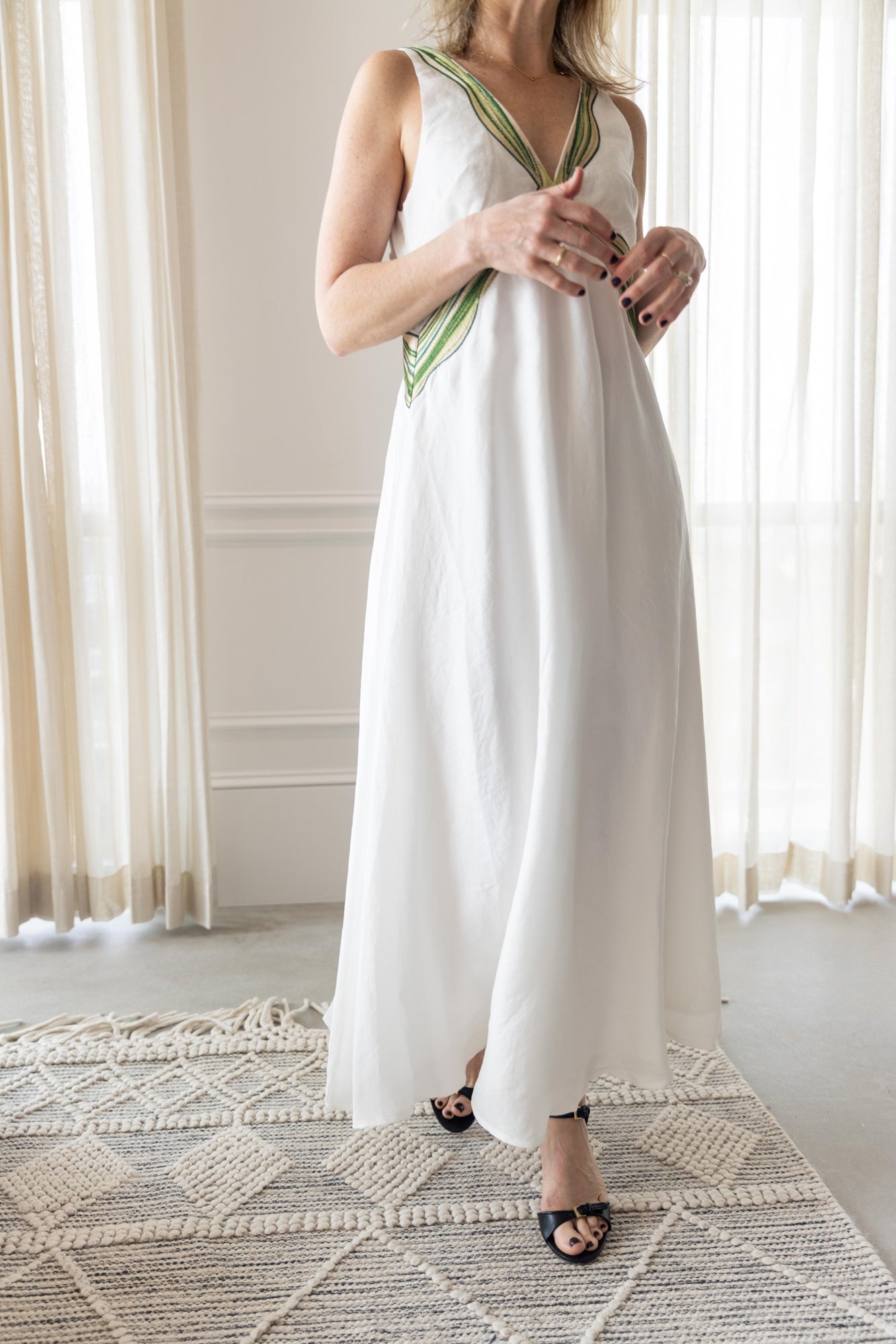 Woman wearing the sancia rhapsody dress in white standing in a room with white curtains.