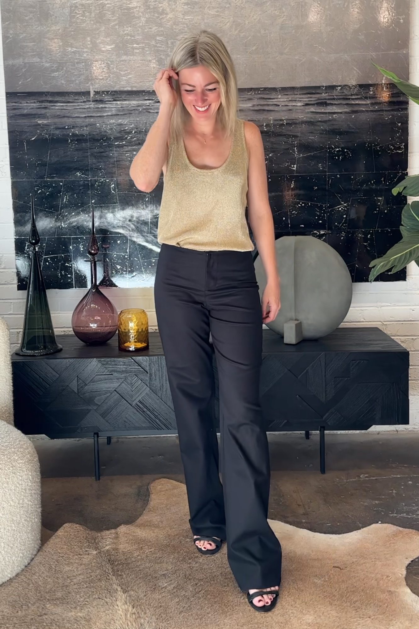 Woman in a gold top and black pants standing in a living room.