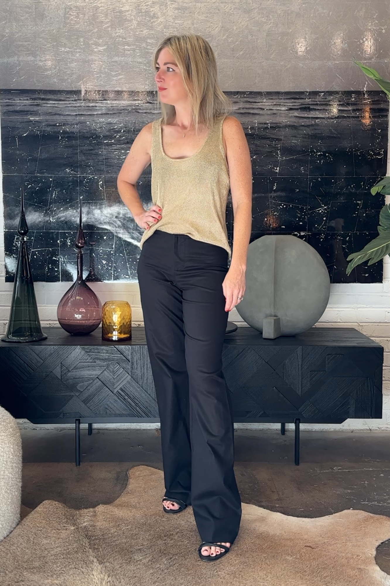 Woman standing in a modern living room with decorative vases on a shelf.