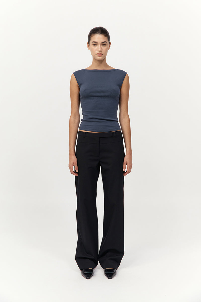 Person wearing a dark blue sleeveless top and black pants on a white background