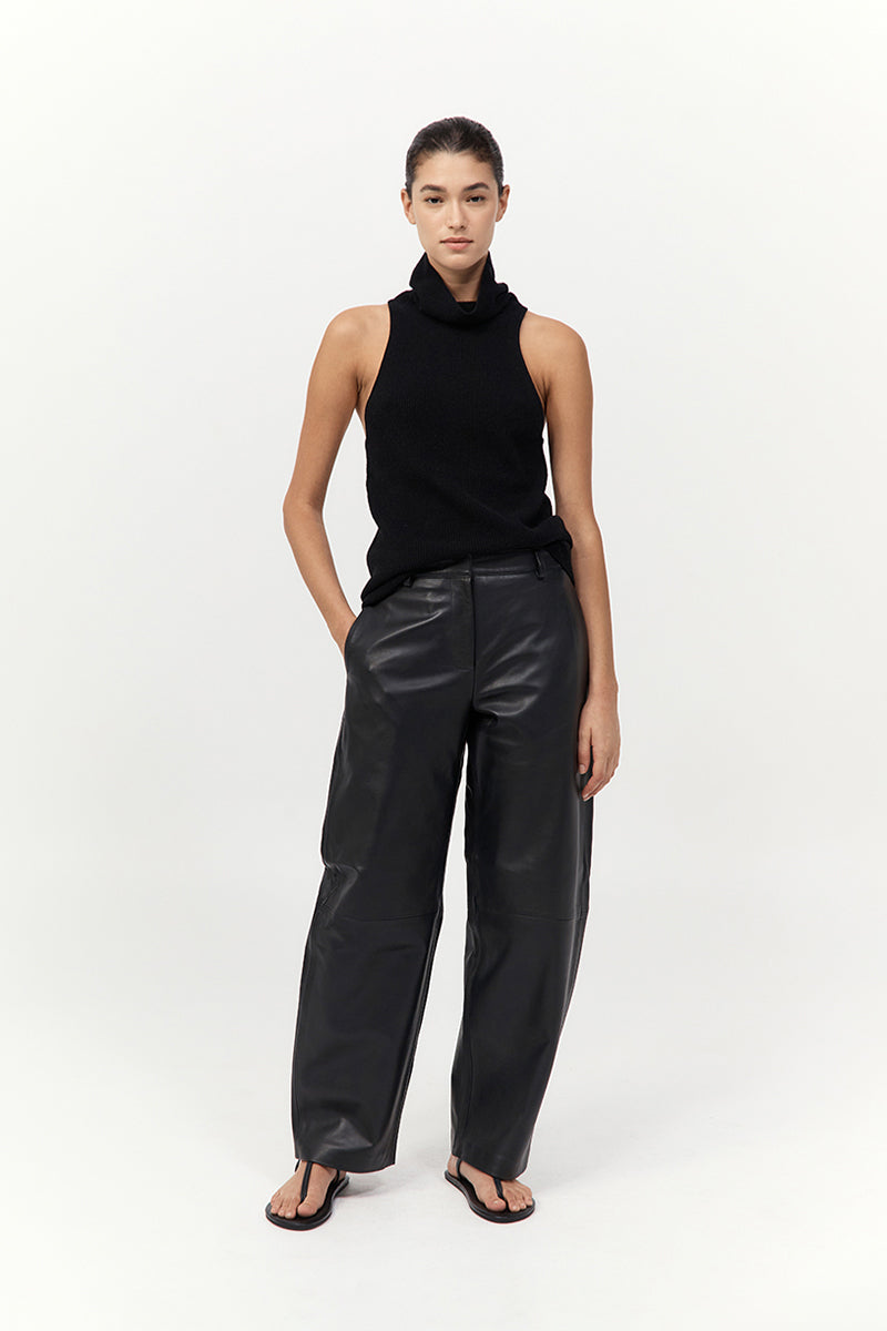 Person wearing a black sleeveless top and leather pants on a white background