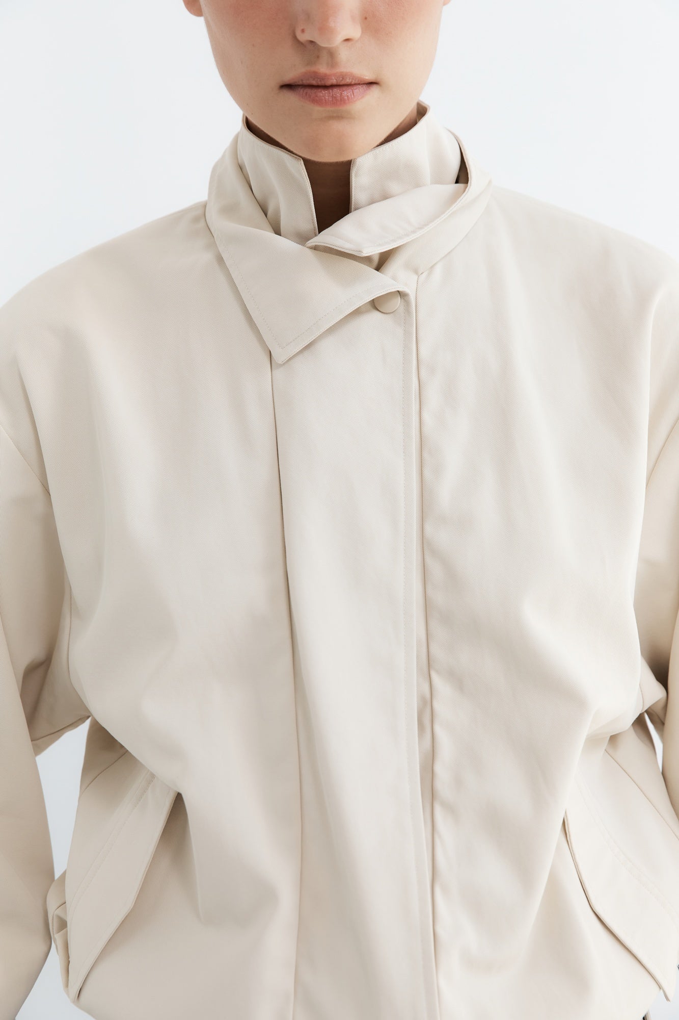 Close-up of a person wearing a beige coat with a white background