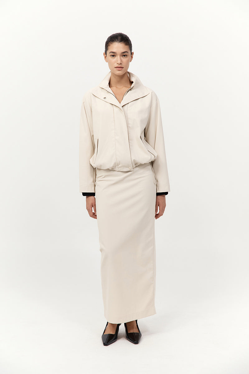 Person wearing a beige outfit with a jacket and skirt on a white background