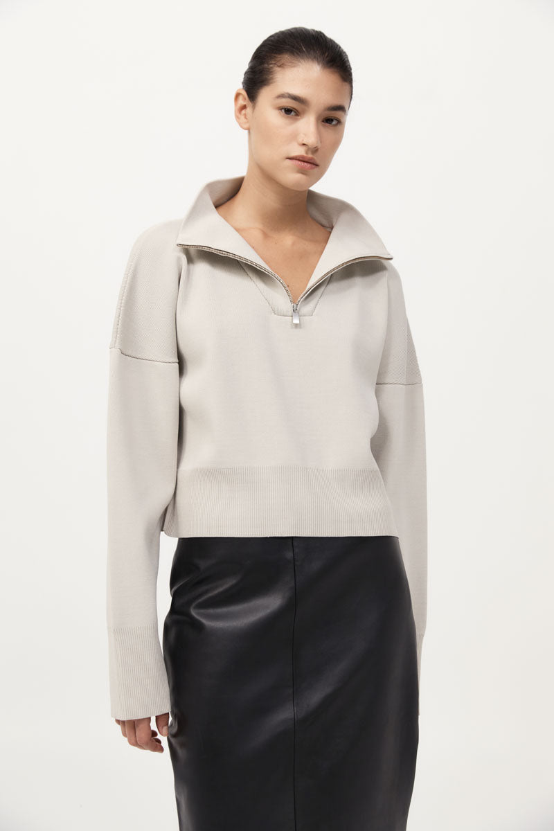 Woman wearing a light gray jacket and black skirt on a white background