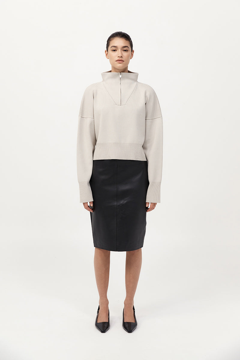 Person wearing a beige sweater and black skirt on a white background