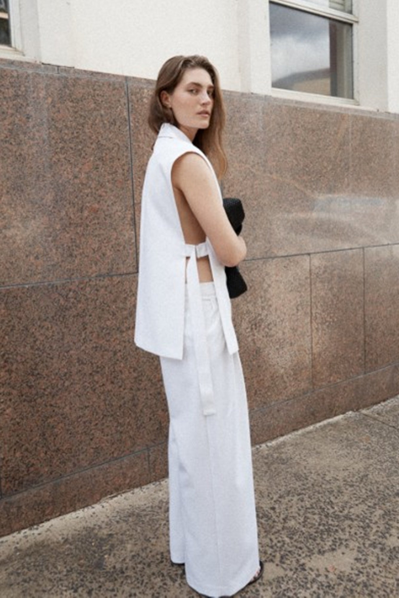 Woman in a white outfit standing against a brown wall.