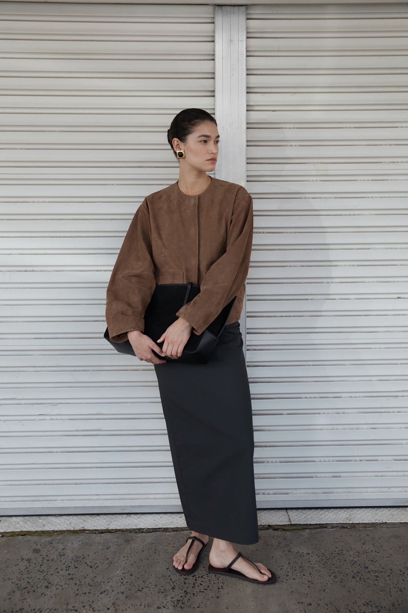 Woman in a brown jacket and black skirt standing in front of a white shutter.