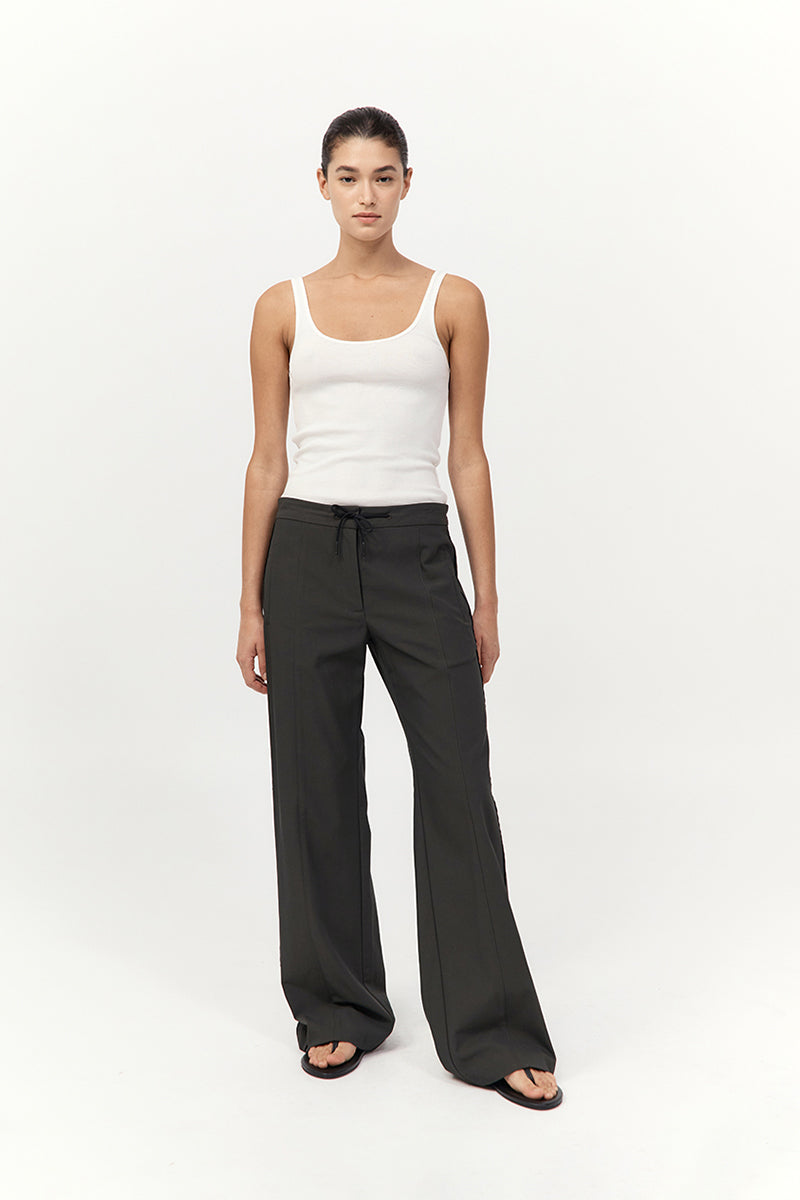 Woman wearing a white tank top and dark gray wide-leg pants on a white background