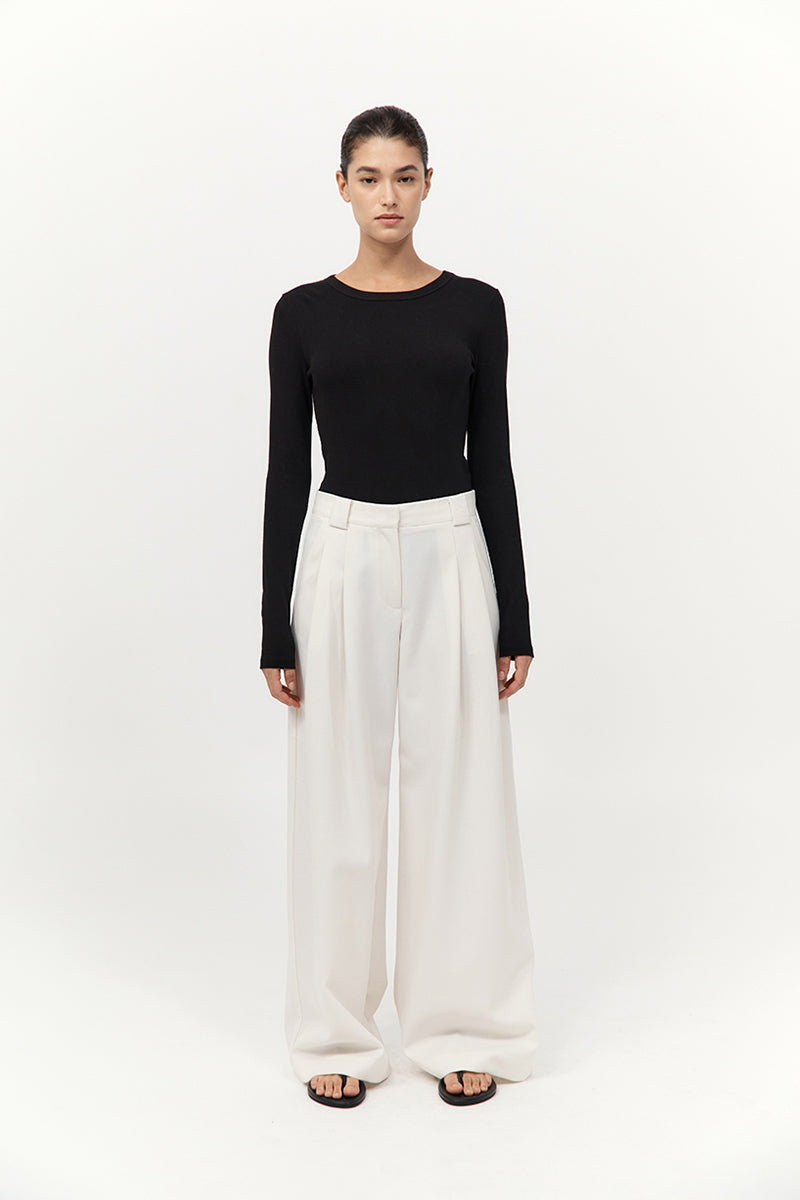 Person wearing a black long-sleeve top and white wide-leg pants on a white background