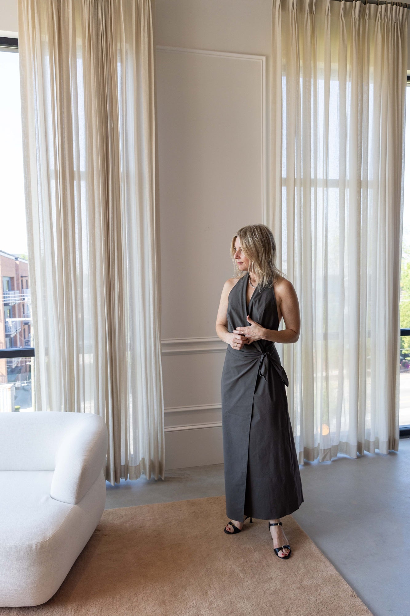 Woman wearing the St Agni Halter Wrap Backless Dress standing against white curtains