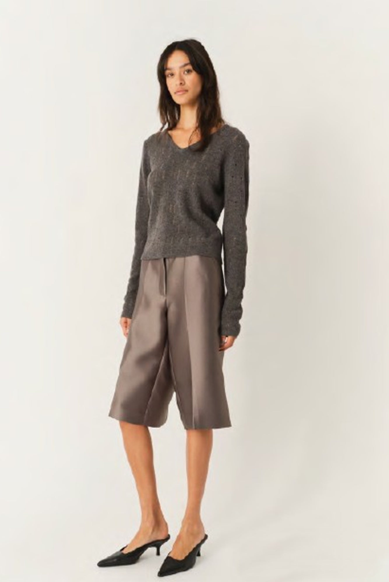 Woman wearing a gray sweater and brown shorts on a white background