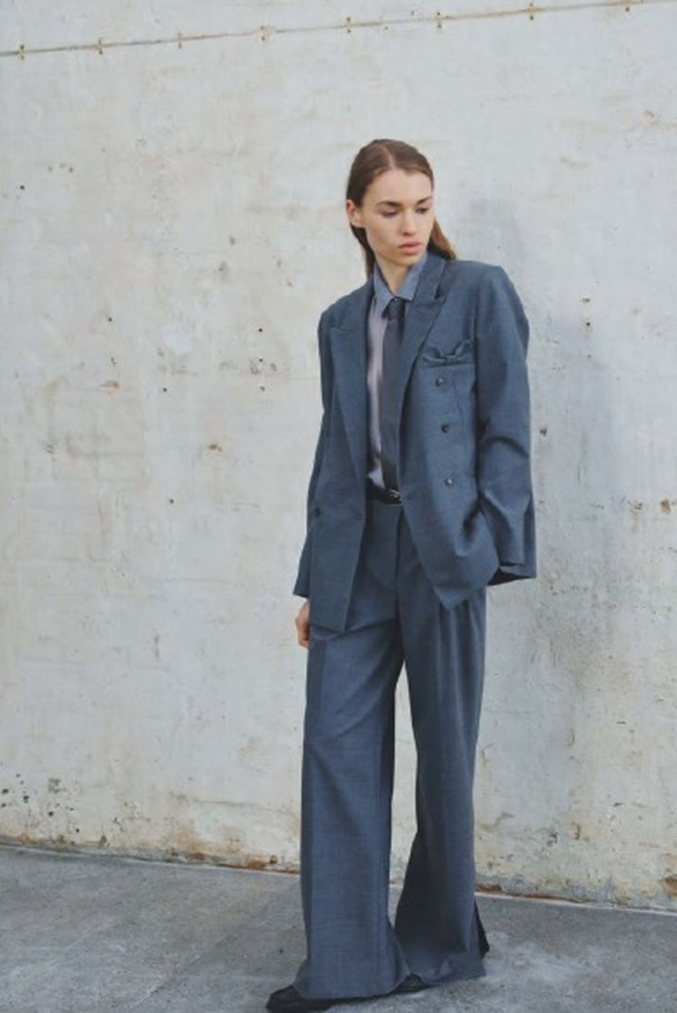 Person wearing a gray suit standing against a plain wall.
