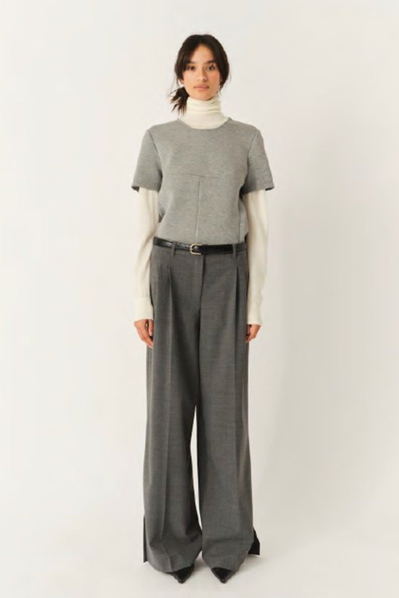 Person wearing a gray sweater and wide-leg pants on a white background