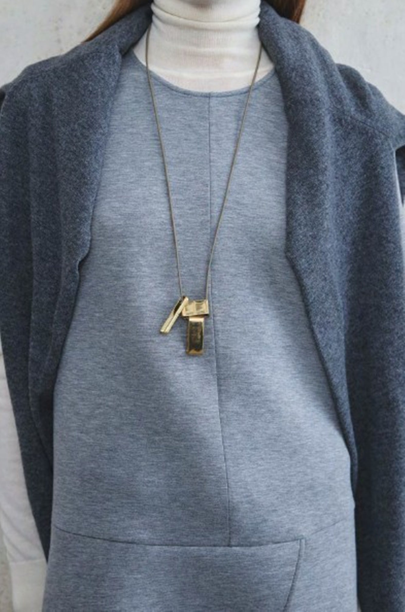 Person wearing a gray outfit with a long necklace featuring a key pendant.