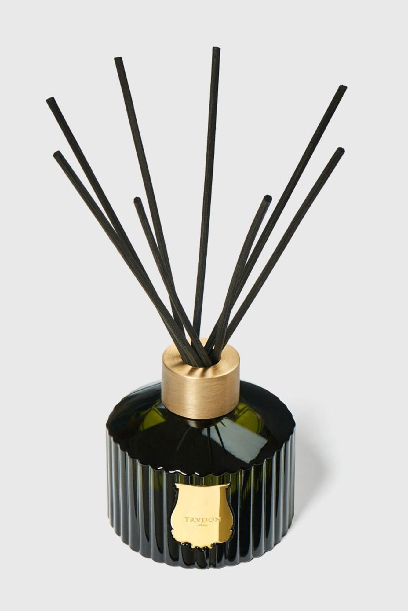 Black reed diffuser with gold accents on a light gray background